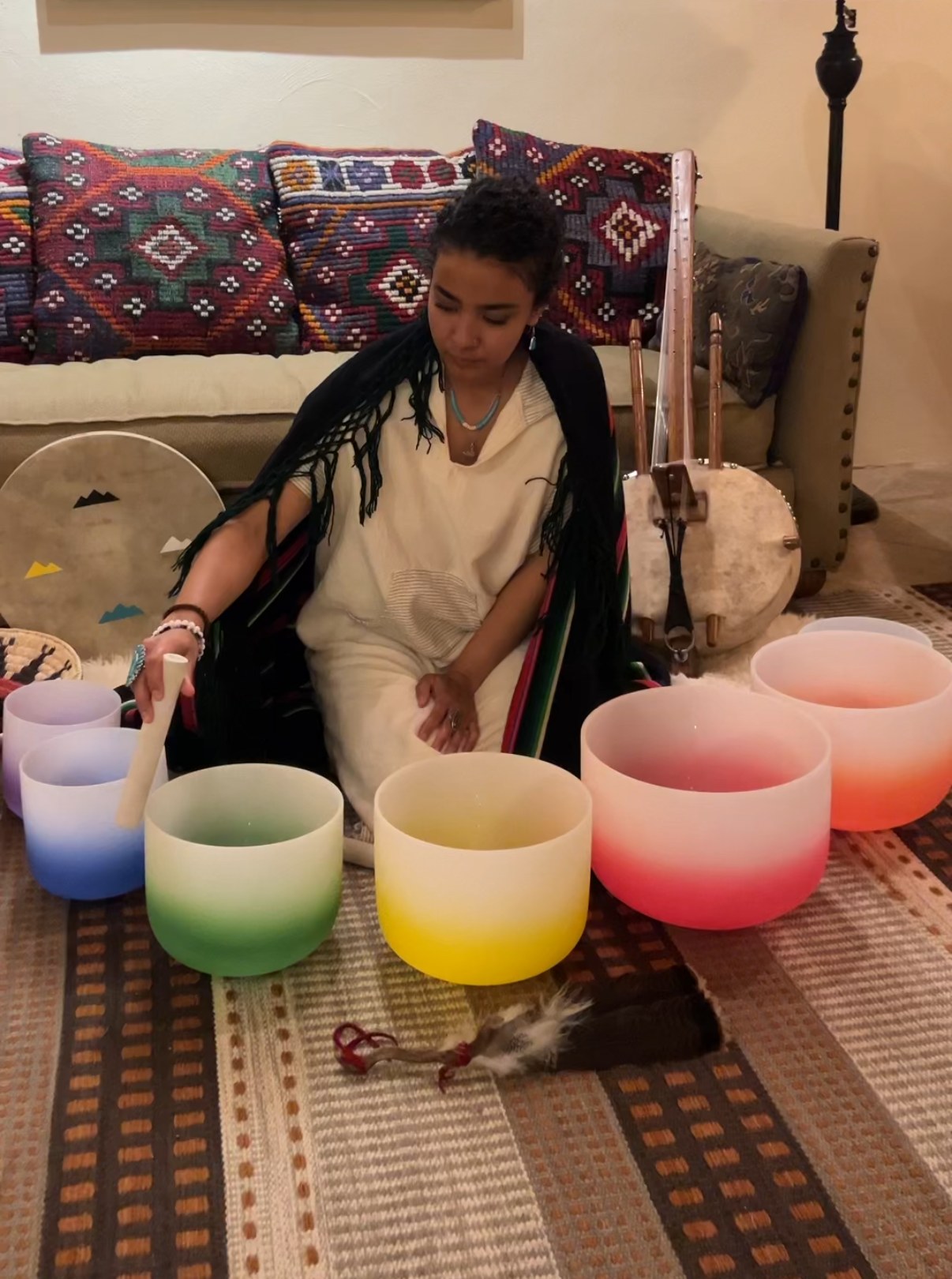 Deoné seated on a woven rug playing crystal singing bowls, with a kora and a hand drum beside her