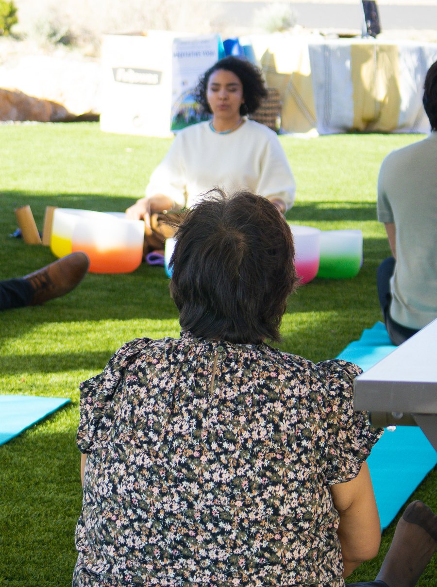 Deoné leading a sound journey outdoors with crystal singing bowls, participants seated on mats