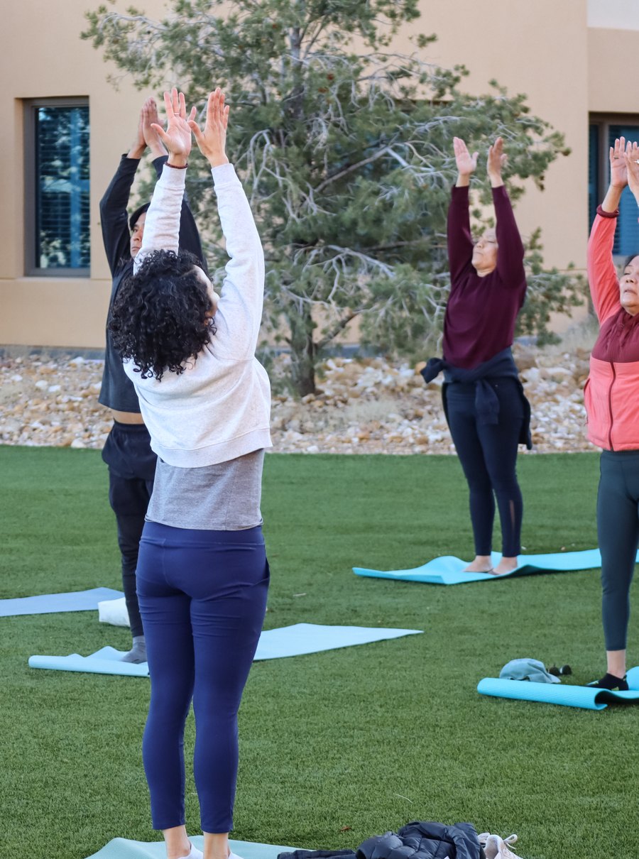 Deoné leading an outdoor group yoga class, everyone reaching their arms overhead